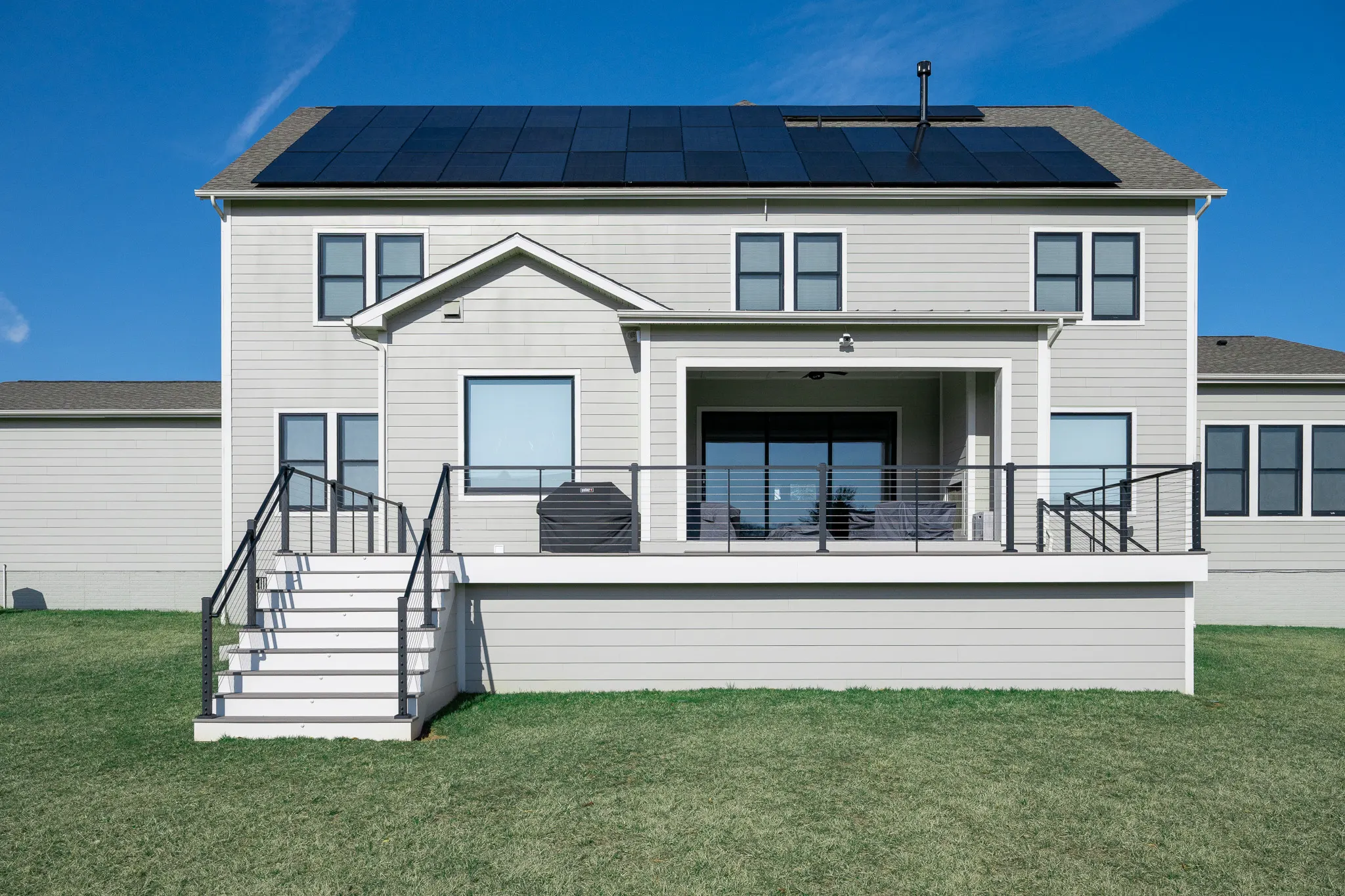 Modern composite deck with black cable railing across the back of a white house